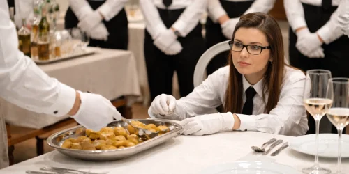 Silver service training demonstration showing a waiter serving food from a platter in formal dining service